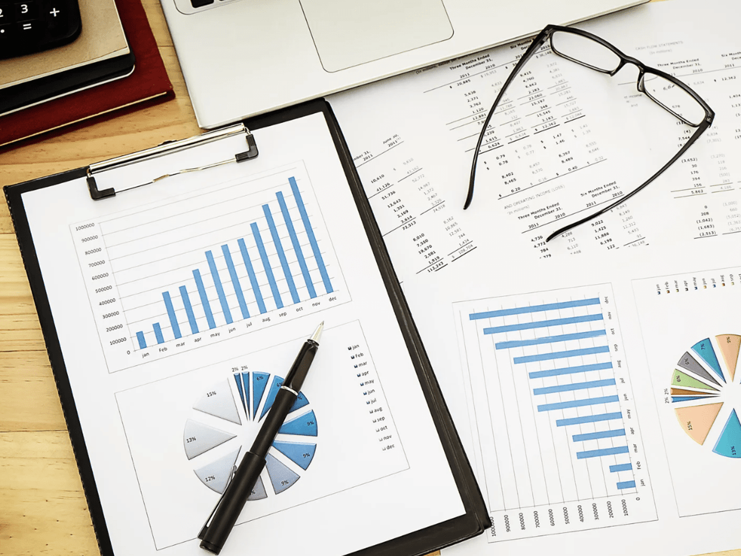 Charts and graphs on a desk with glasses and a laptop